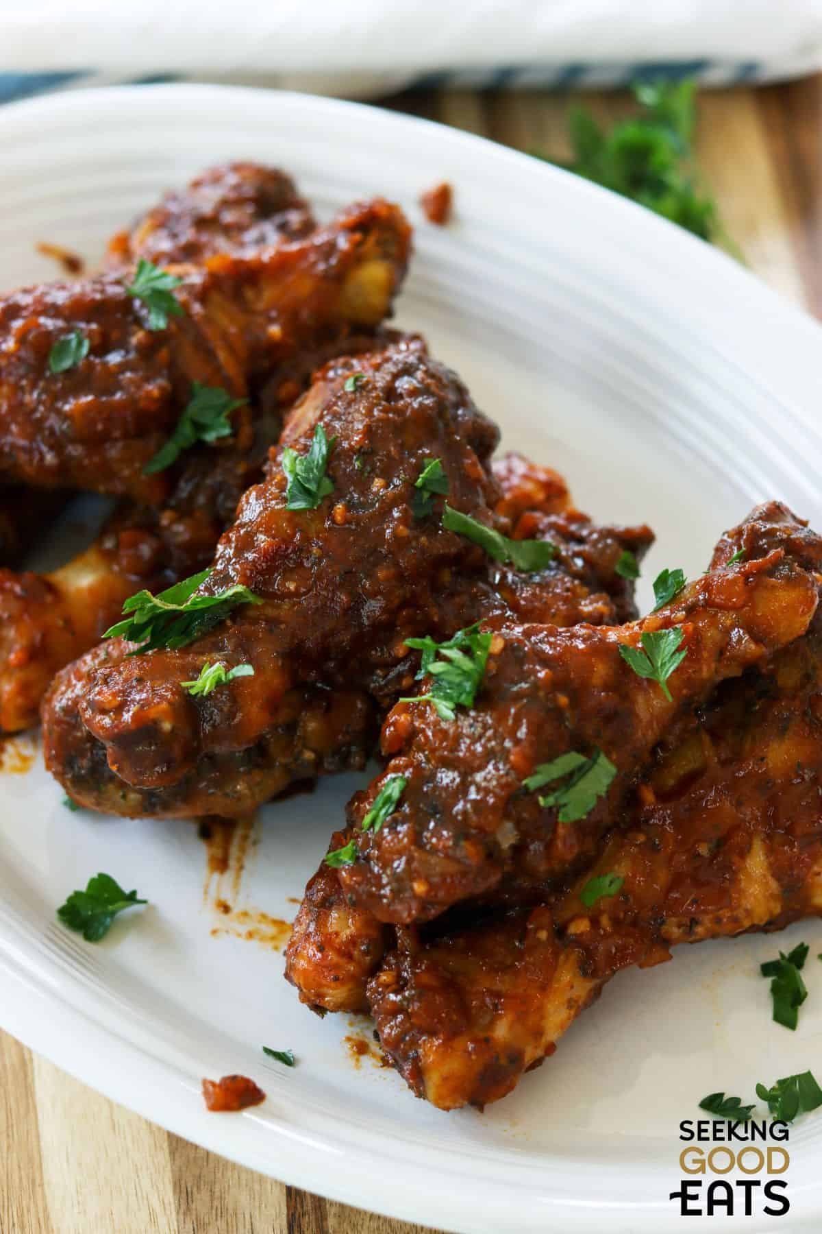 Plate of saucy oven baked chicken drumsticks on a white plate.