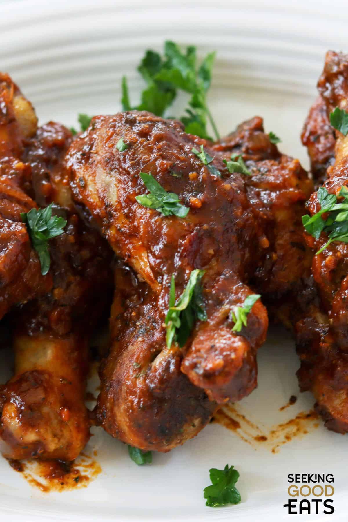 Plate of BBQ chicken drumsticks on white plate.