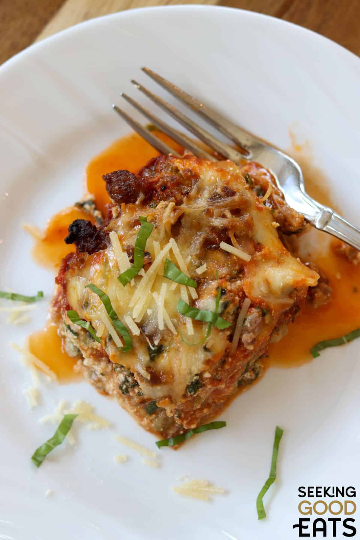 Piece of eggplant lasagna with sausage served on a white plate with a fork.