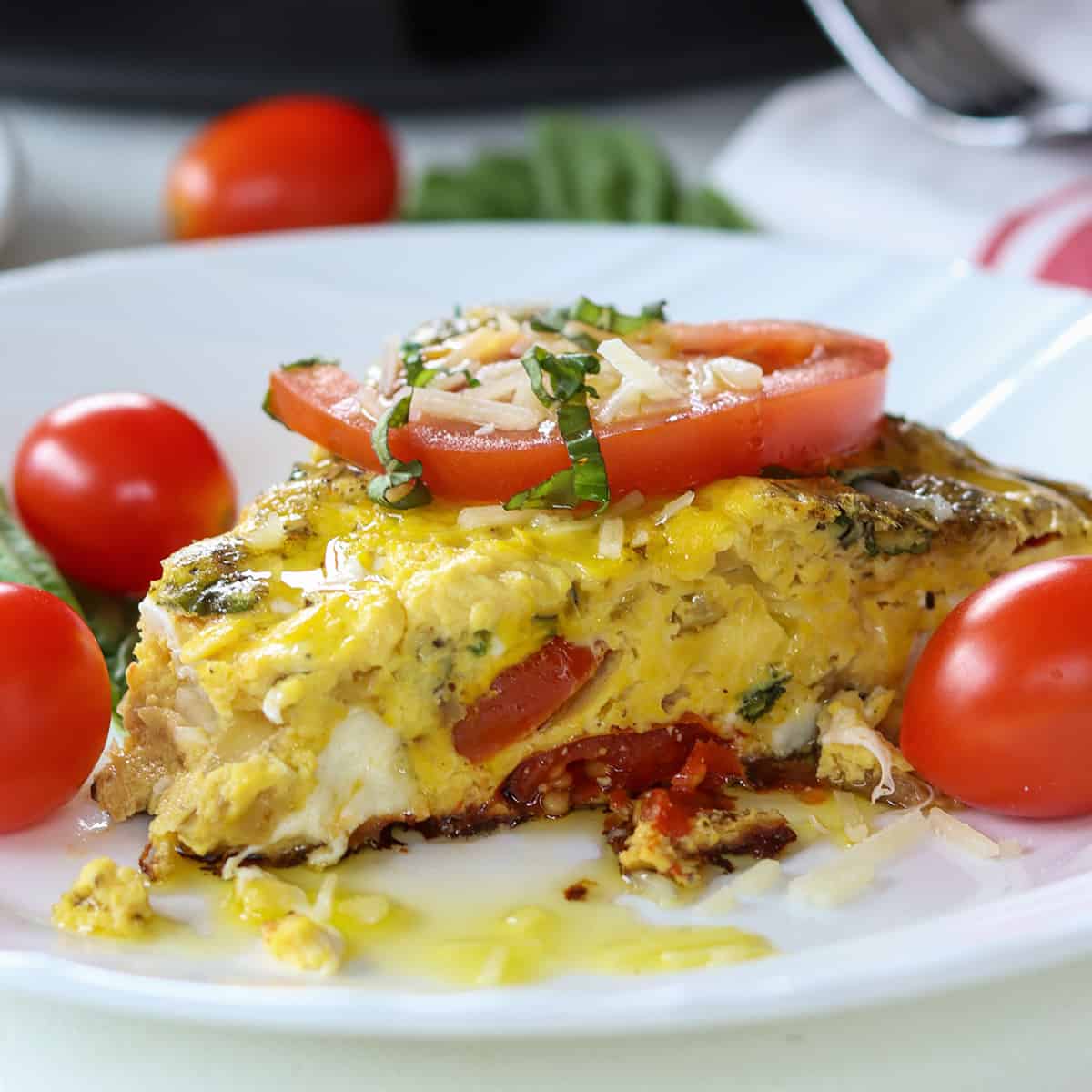 Square image closeup of a slice of tomato mozzarella caprese frittata on a white plate garnished with basil, tomato, and cheese