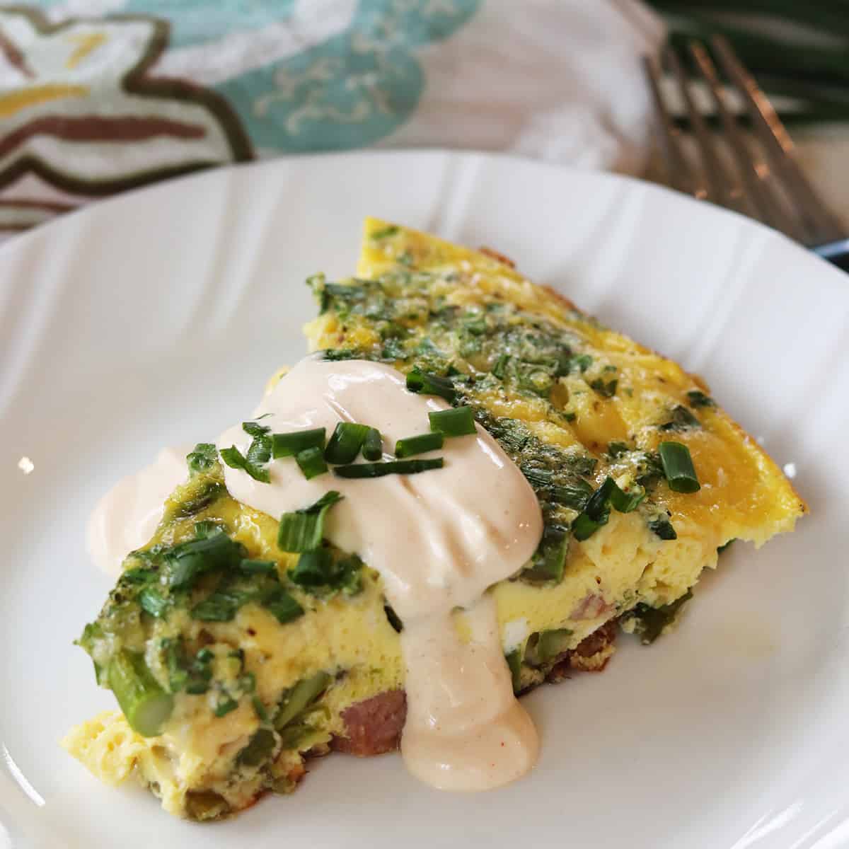 Square feature image of eggs benedict frittata served on a white plate and garnished with hollandaise and chives.