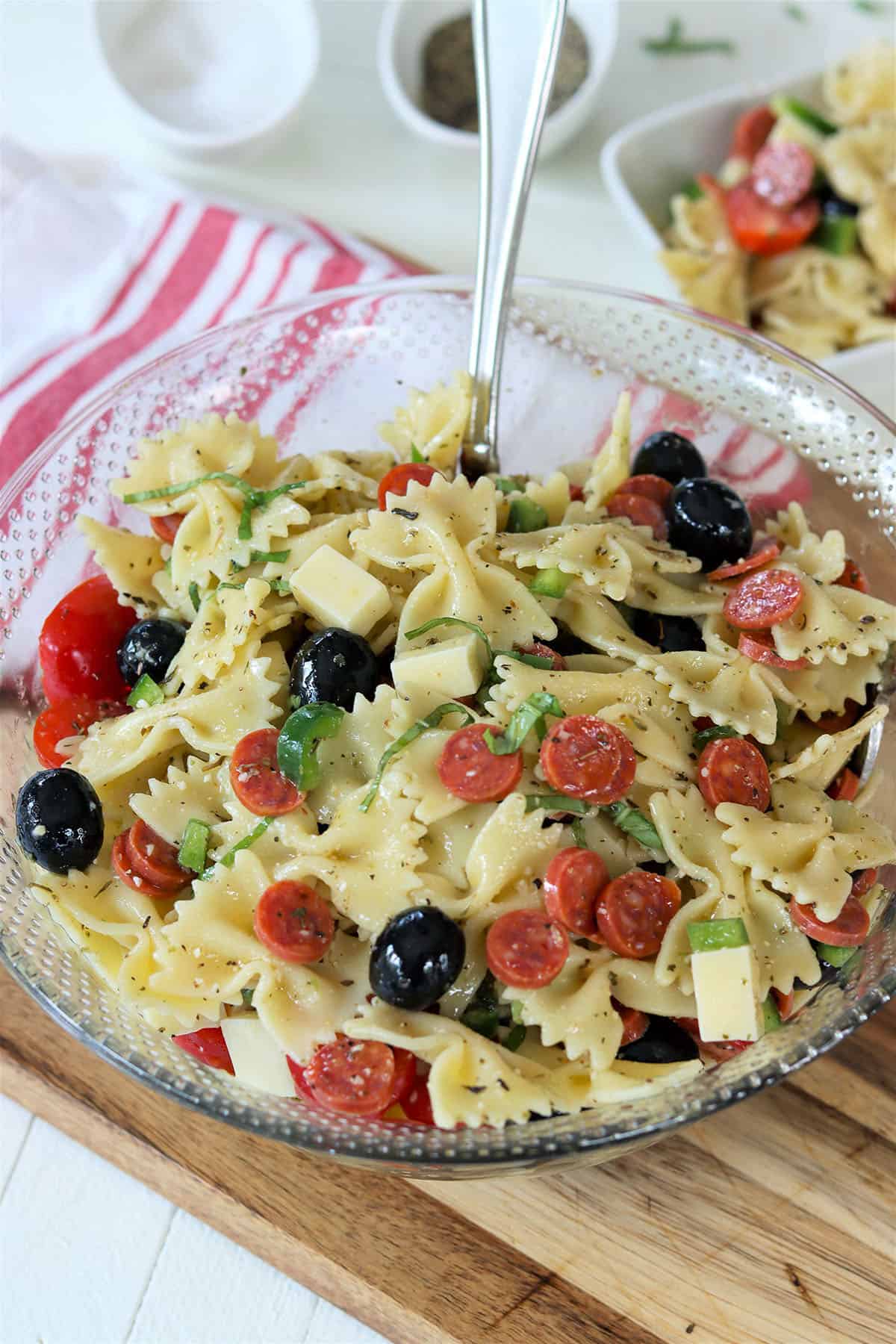 A clear glass bowl full of italian pasta salad garnished with fresh basil