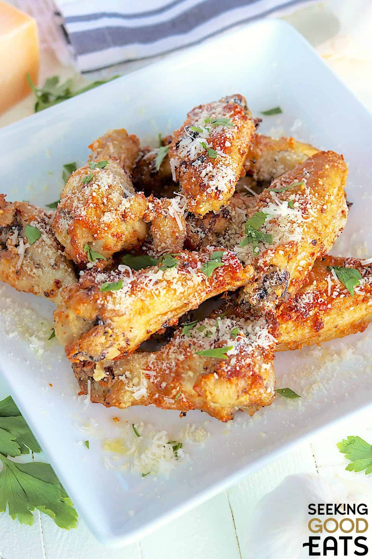 Garlic parmesan wings served on a white plate with extra parmesan sprinkled on top.
