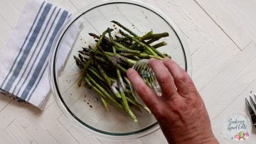 Tossing asparagus spears with seasonings in a clear glass bowl
