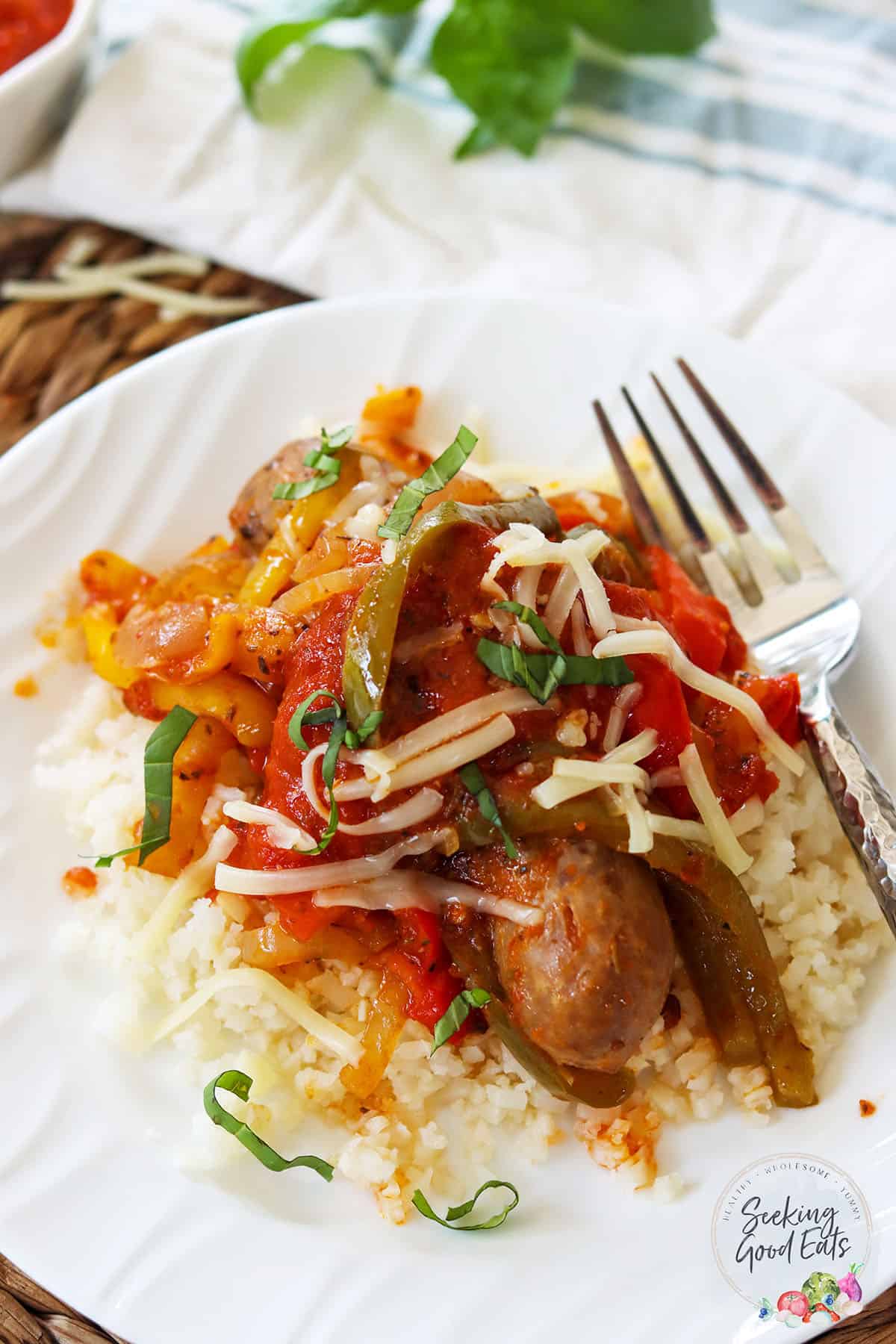 Italian style crockpot sausage and peppers served on a white plate over riced cauliflower.