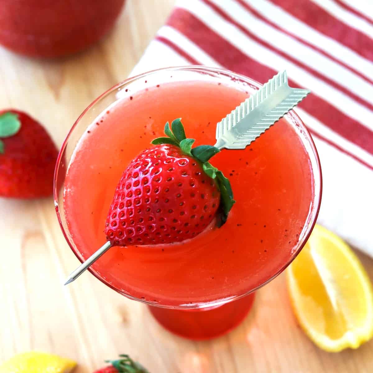 Looking down on a strawberry martini that is garnished with a strawberry skewered with an arrow