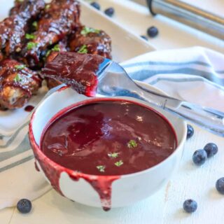 A white bowl of blueberry barbecue sauce and a baster dripping with sauce.