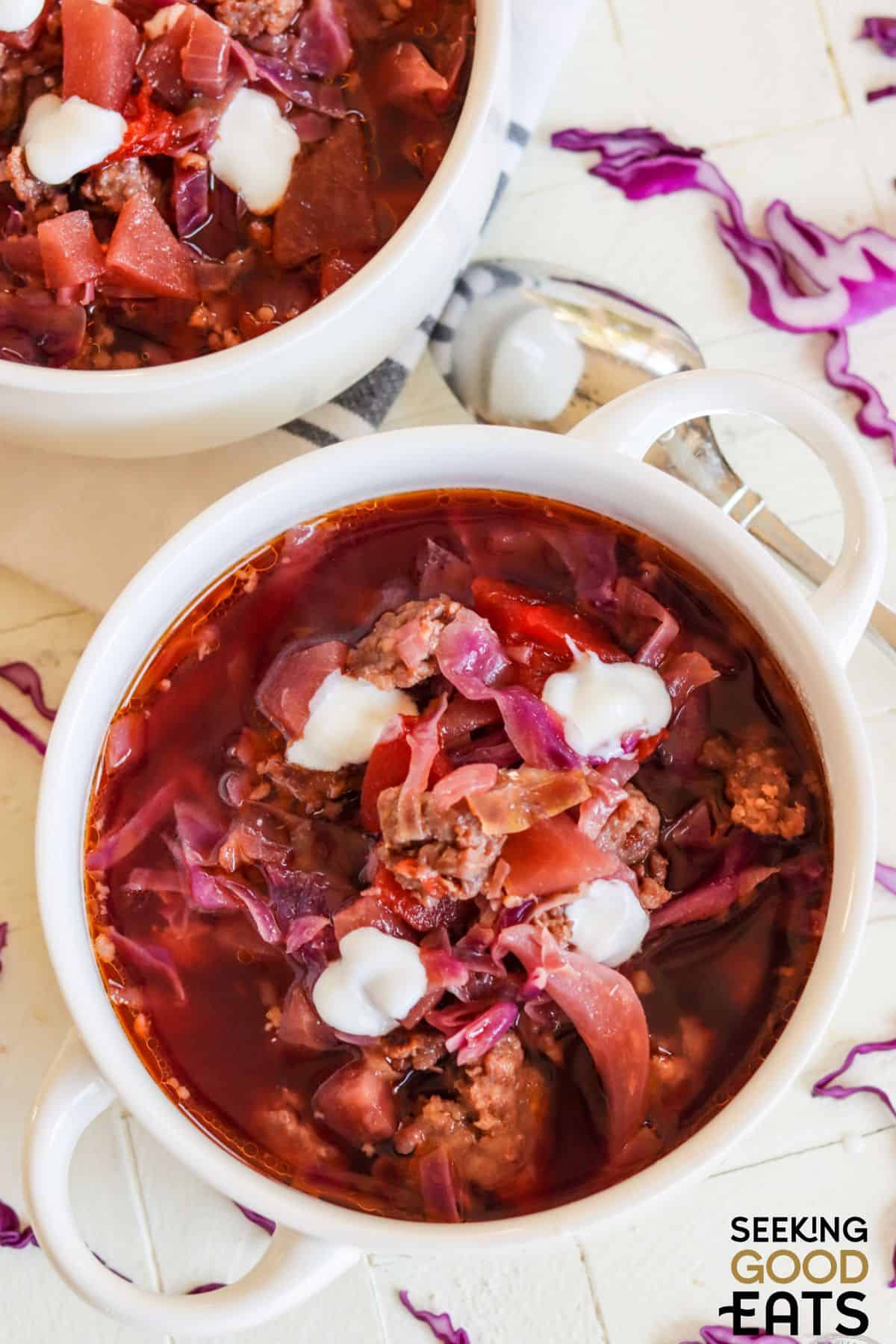 Red cabbage soup with apples and bratwurst served in a white bowl.