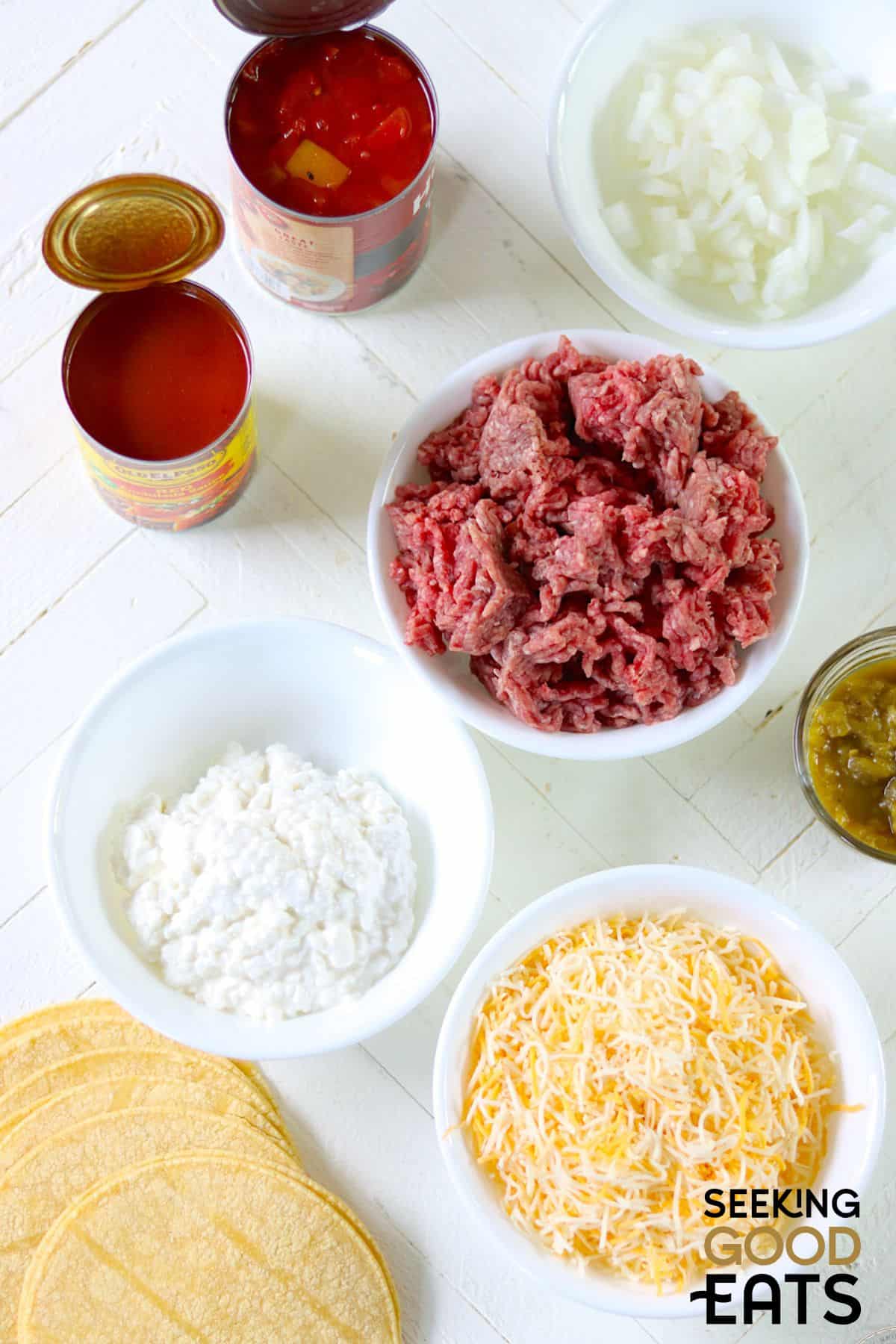 Ingredients needed for making ground beef enchiladas on a white board.