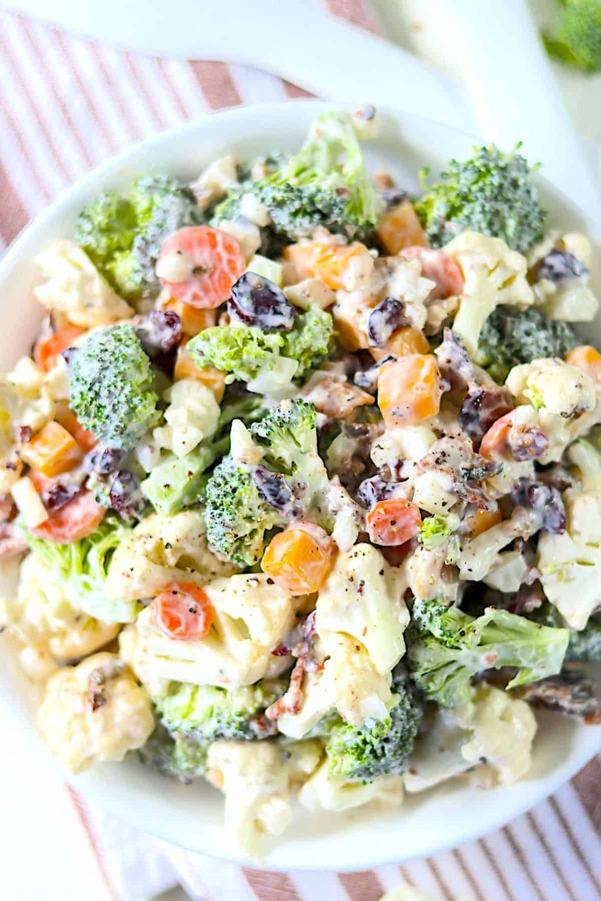 Cauliflower broccoli salad with tangy dressing served in a plain white bowl.