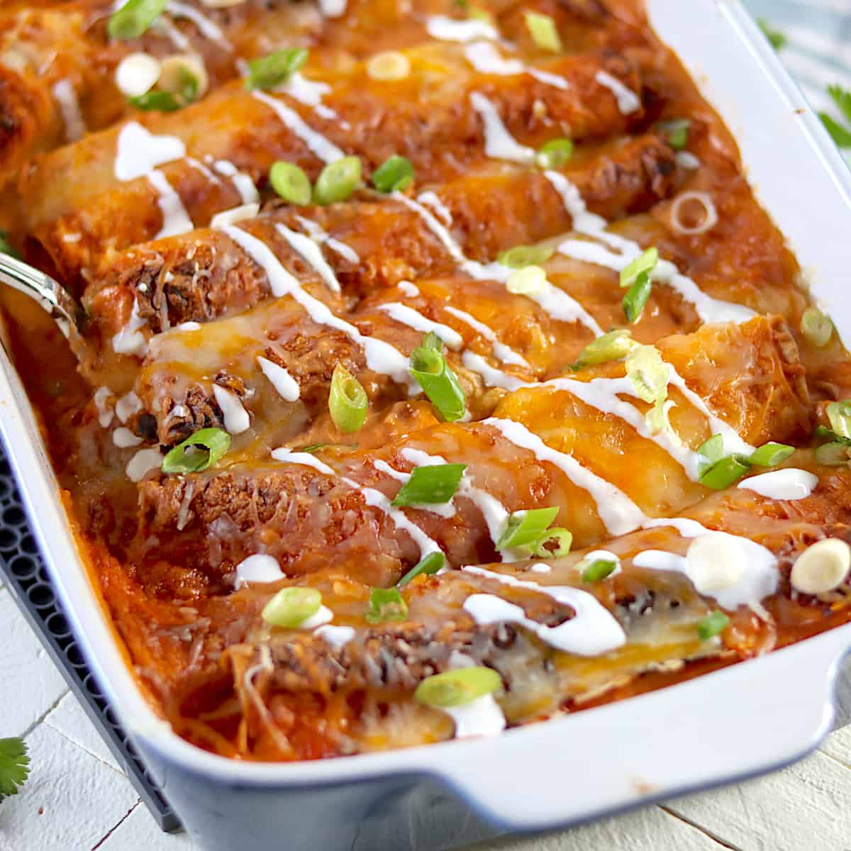 Sour cream is drizzled over the cheesy baked enchiladas in a 13 inch by 9 inch baking dish.