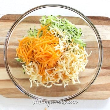 Grated zucchini, grated cheese, and egg in a large clear glass bowl.