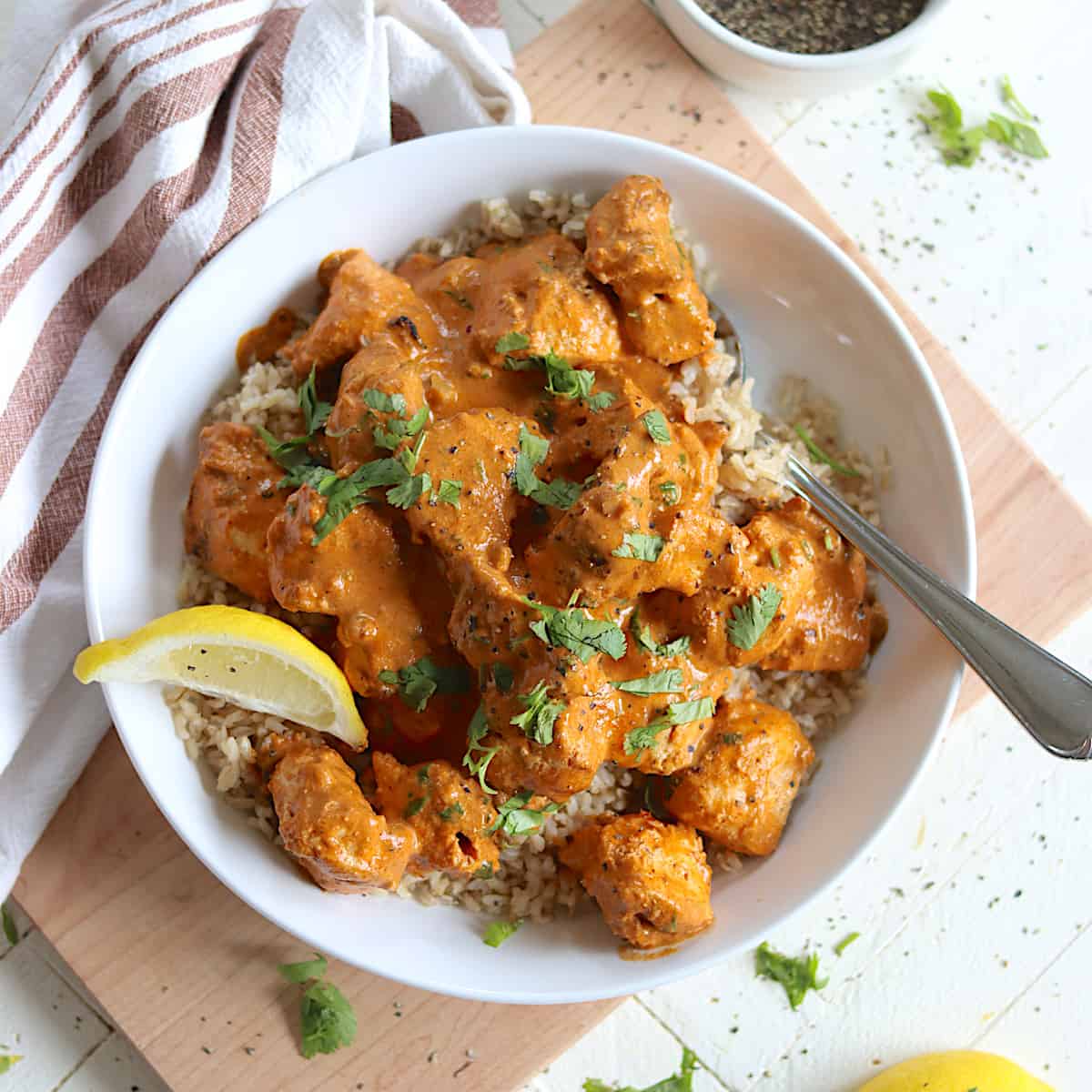 Chunks of chicken tikka masala in a white bowl with creamy sauce over brown rice and garnished with fresh cilantro.