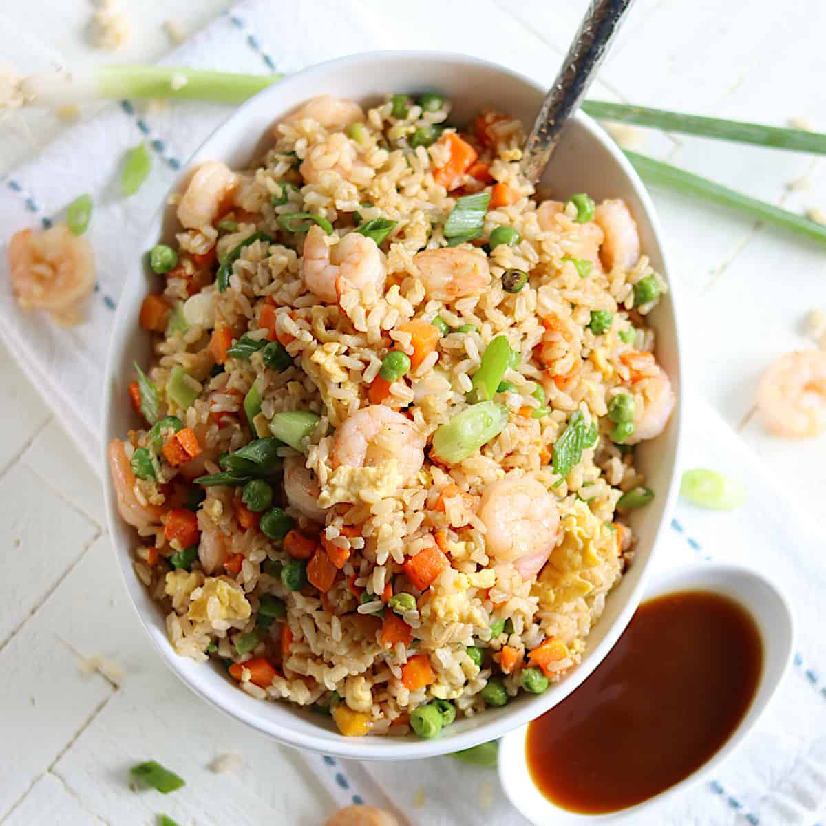 A white bowl of shrimp fried rice with a side of stir fry sauce.
