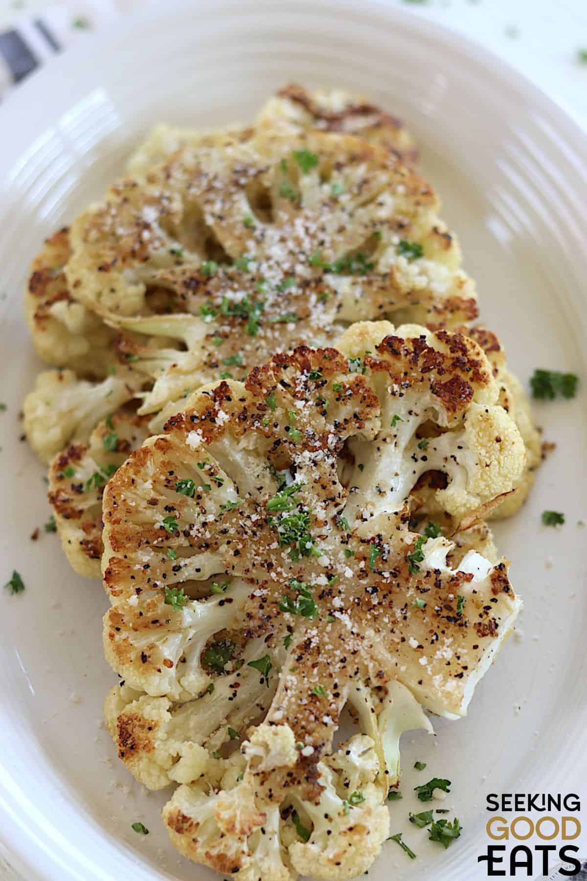 Cooked cauliflower steaks topped with seasoning.