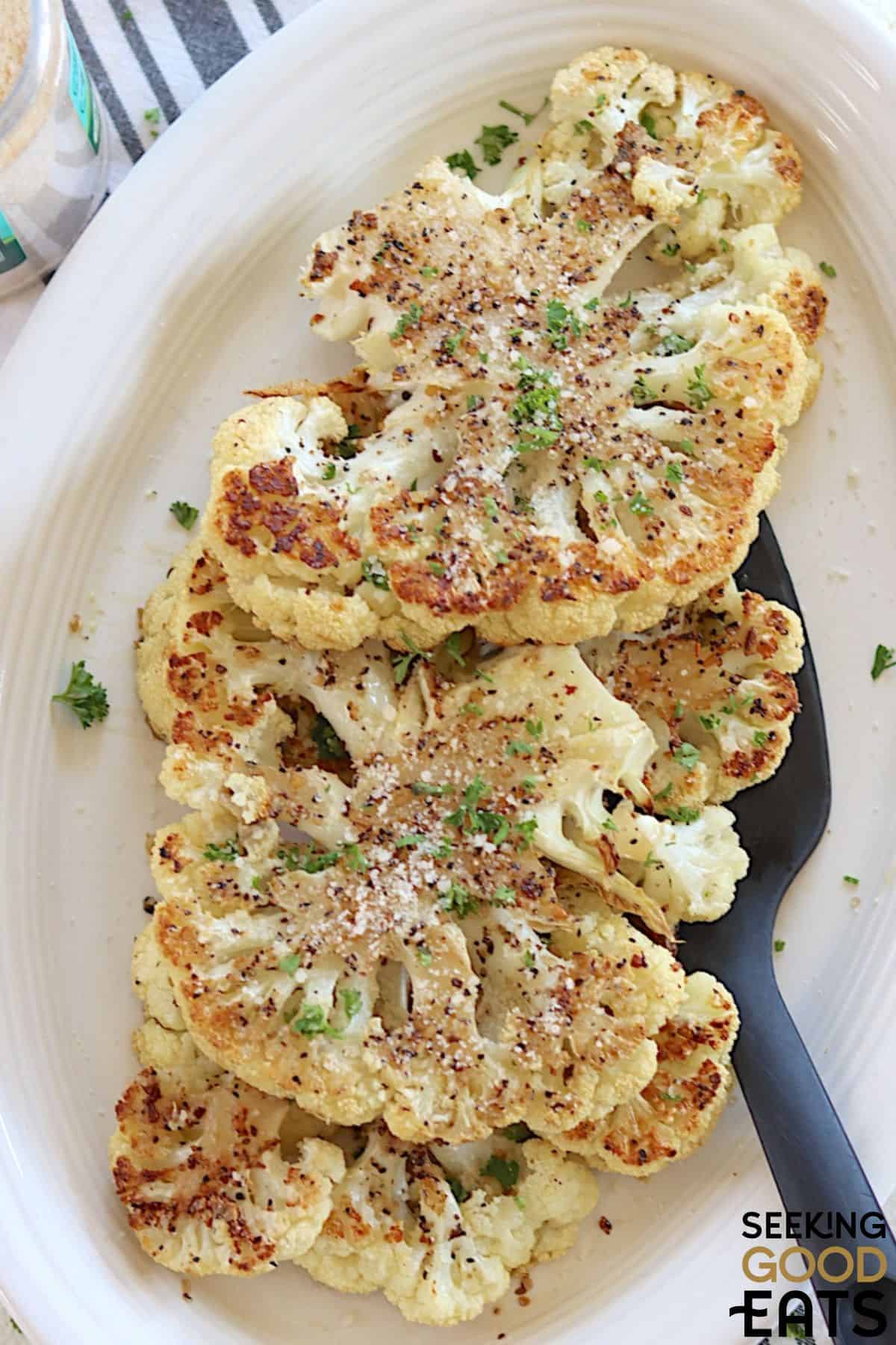 Cooked cauliflower steaks served on a white plate.