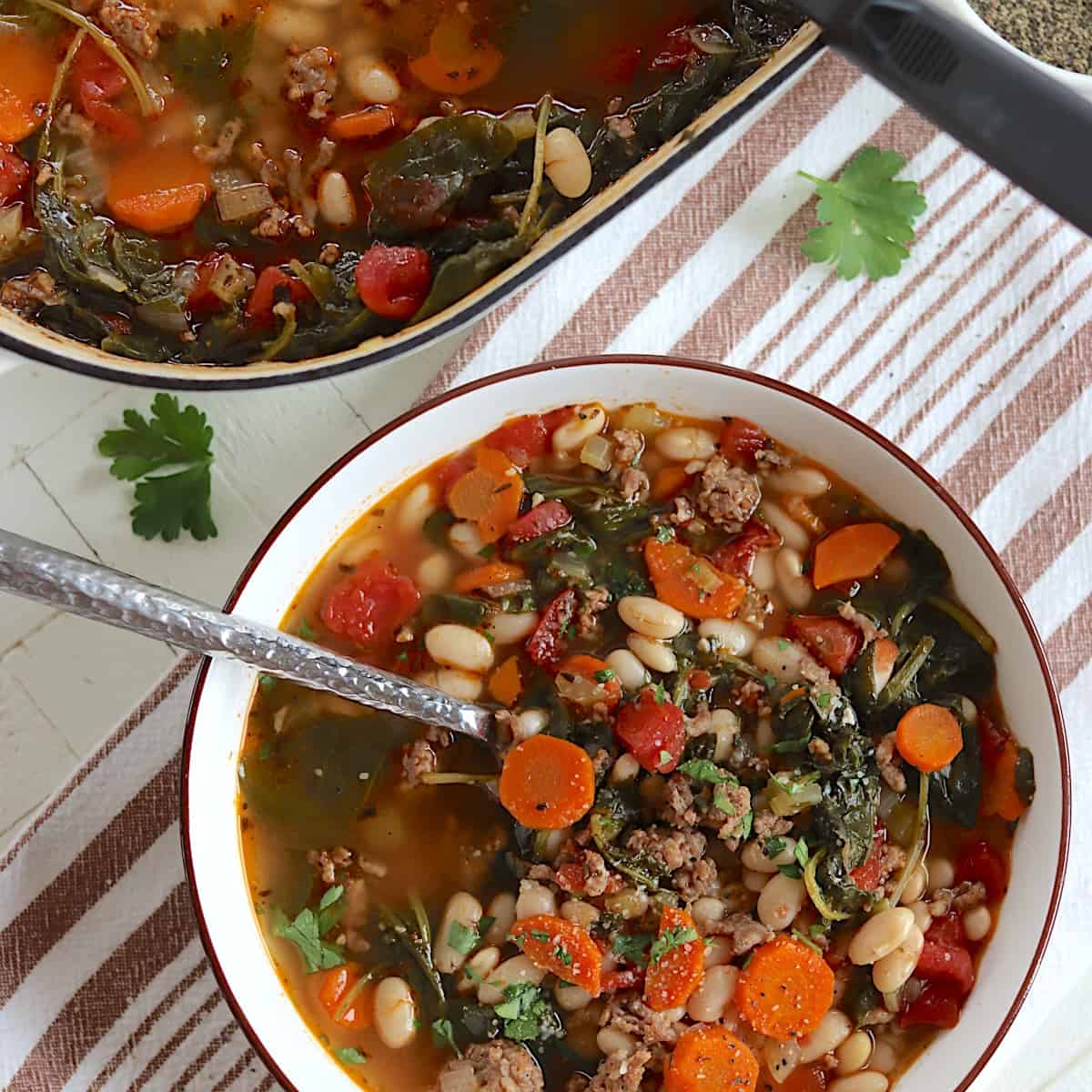 A white bowl of sausage and kale soup with white beans.