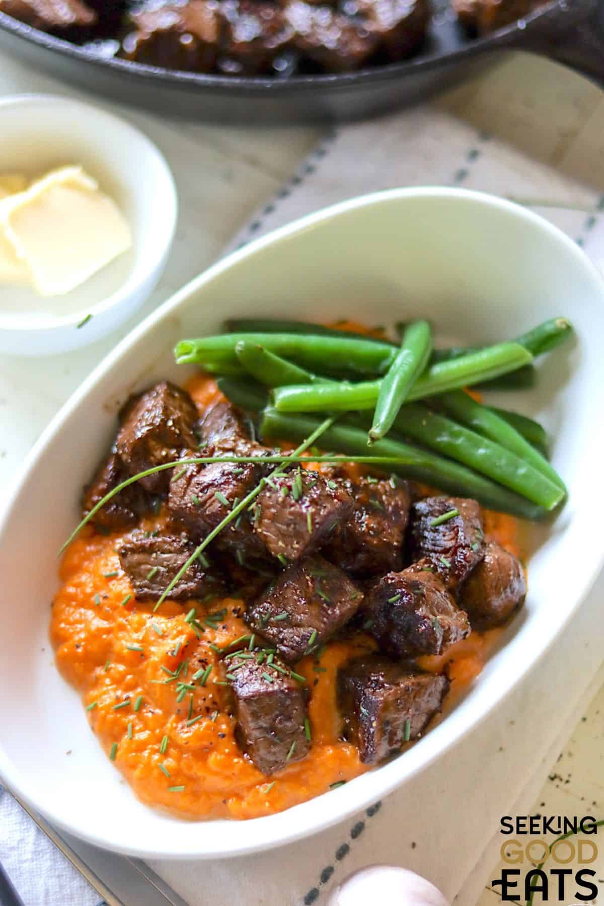 Seated steak bites served with green beans and sauce.