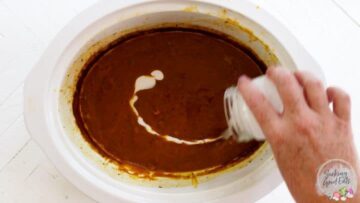 Adding coconut milk to the fully cooked pumpkin soup in a slow cooker.