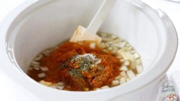 Adding all pumpkin soup ingredients to a large white oval crockpot.