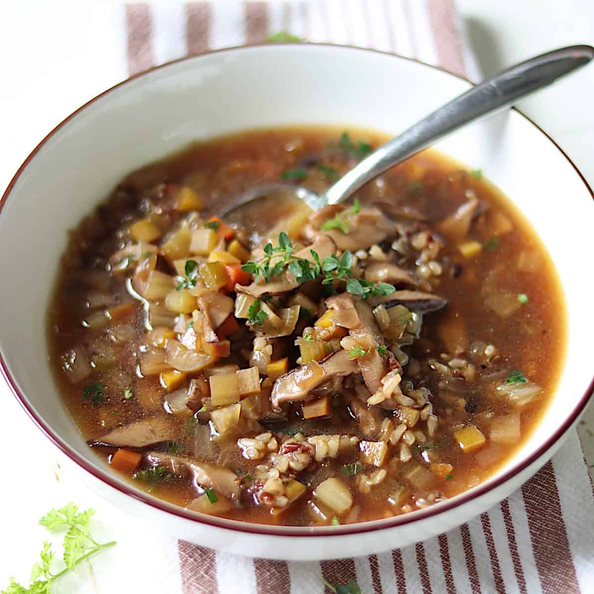 A white bowl of wild rice and mushroom soup garnished with thyme.