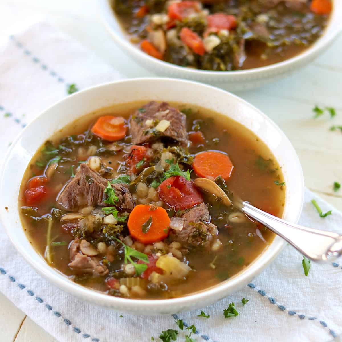 Beef and barley soup with vegetables in a white bowl with a serving spoon.