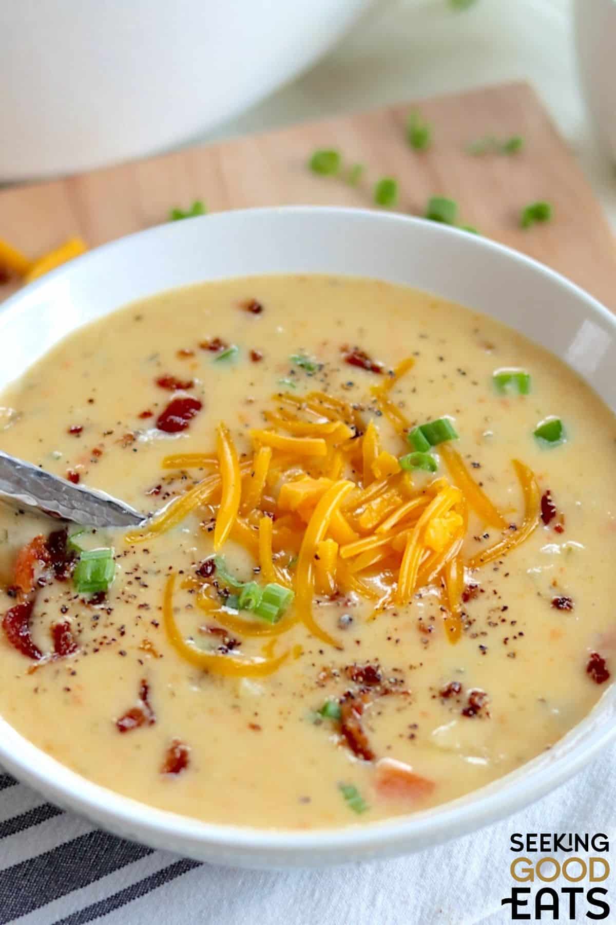 Bowl of cheese and potato soup served with a spoon and extra cheese on top.