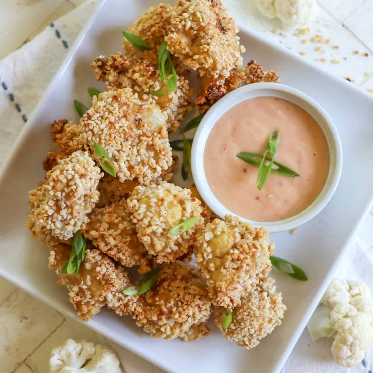 A square plate of bang bang cauliflower and dipping sauce.