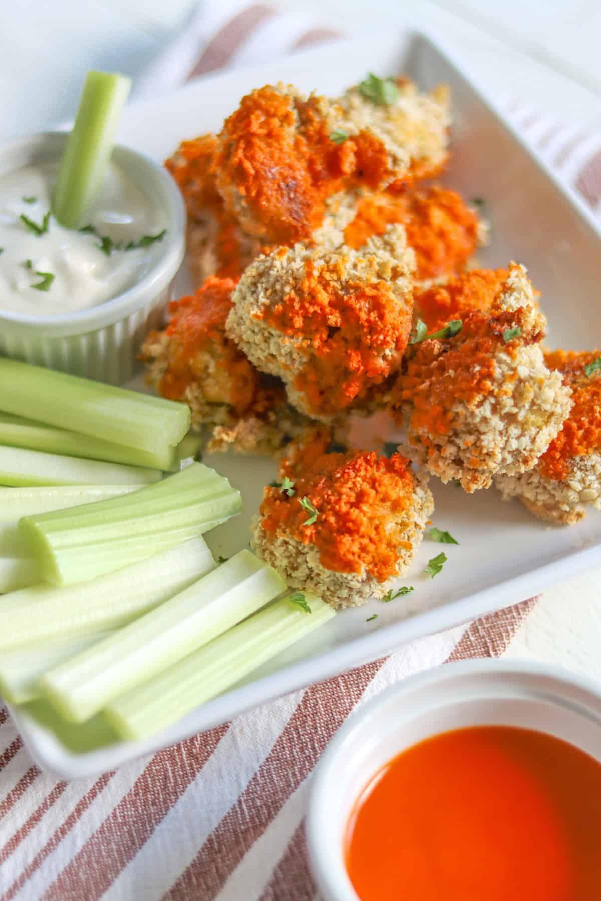 A white square plate with cauliflower wings drizzled with buffalo sauce with a side of blue cheese dressing.