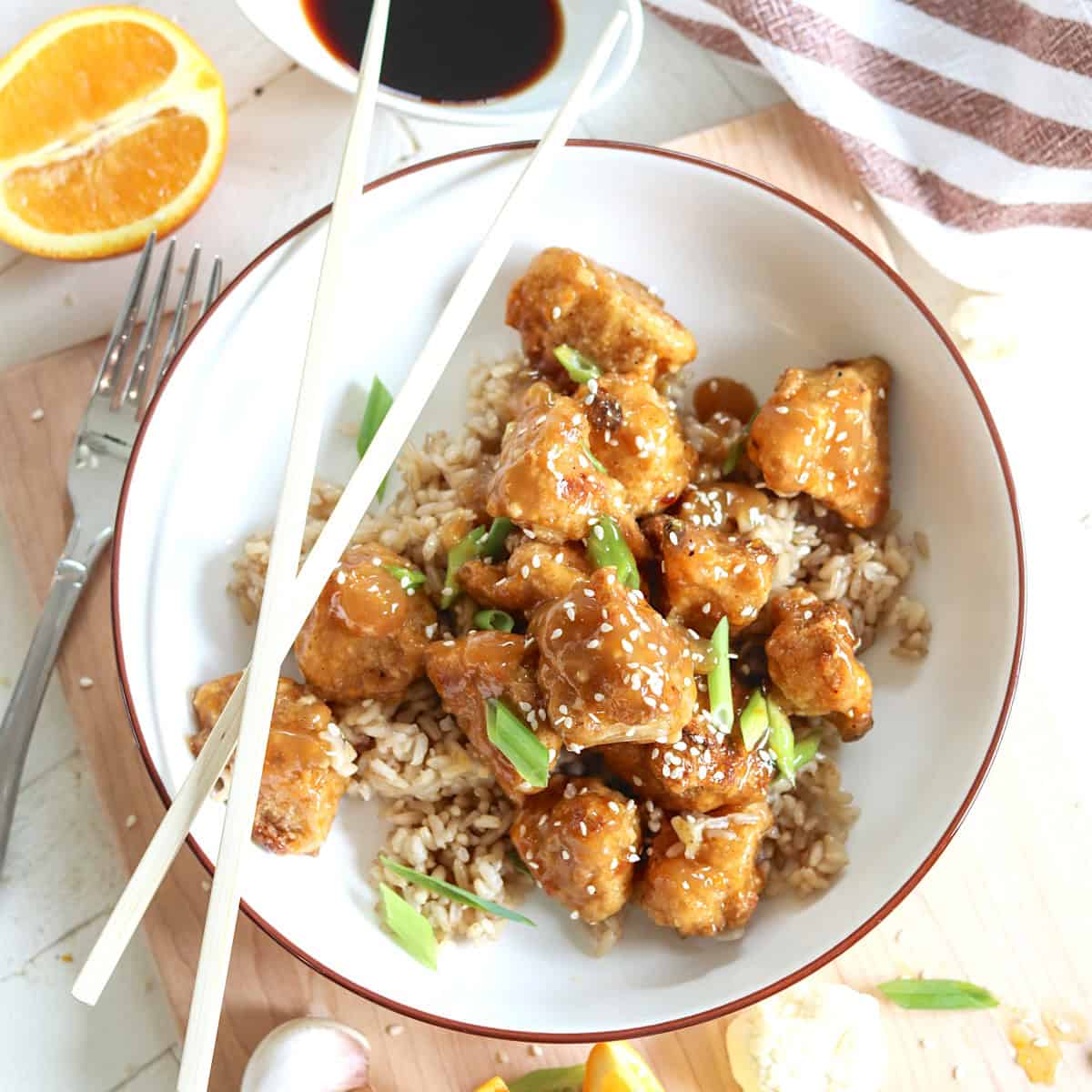 A white bowl of orange cauliflower over brown rice.