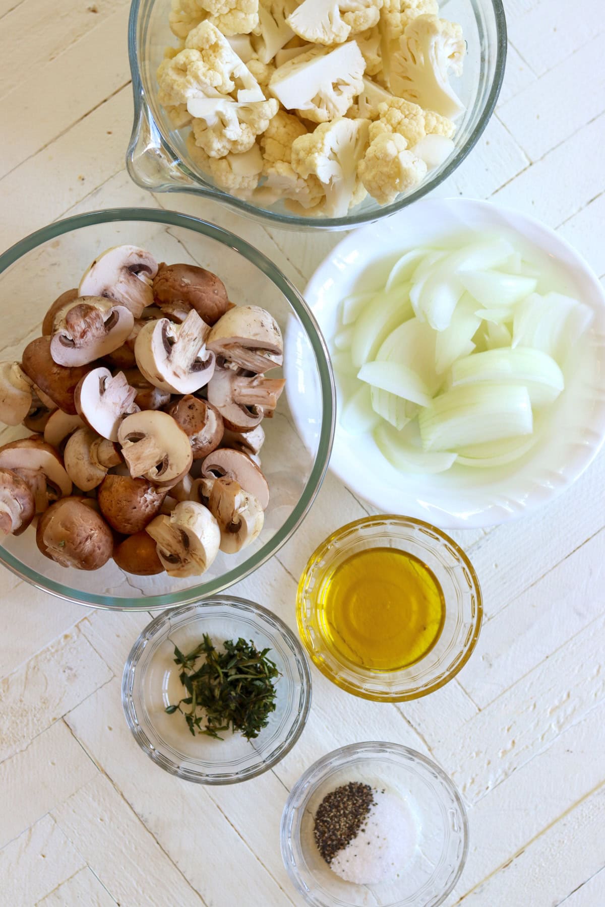 Ingredients need for making cauliflower and mushrooms on a white wooden board.