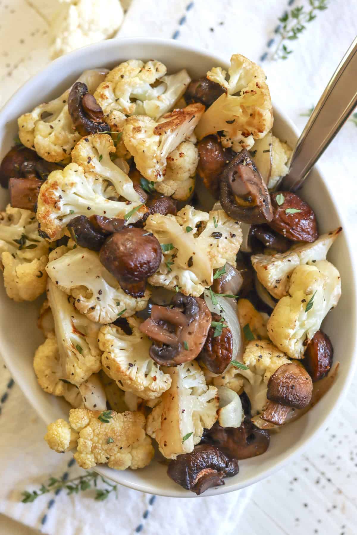 An oval white serving dish of roasted mushrooms and cauliflower with fresh herbs.