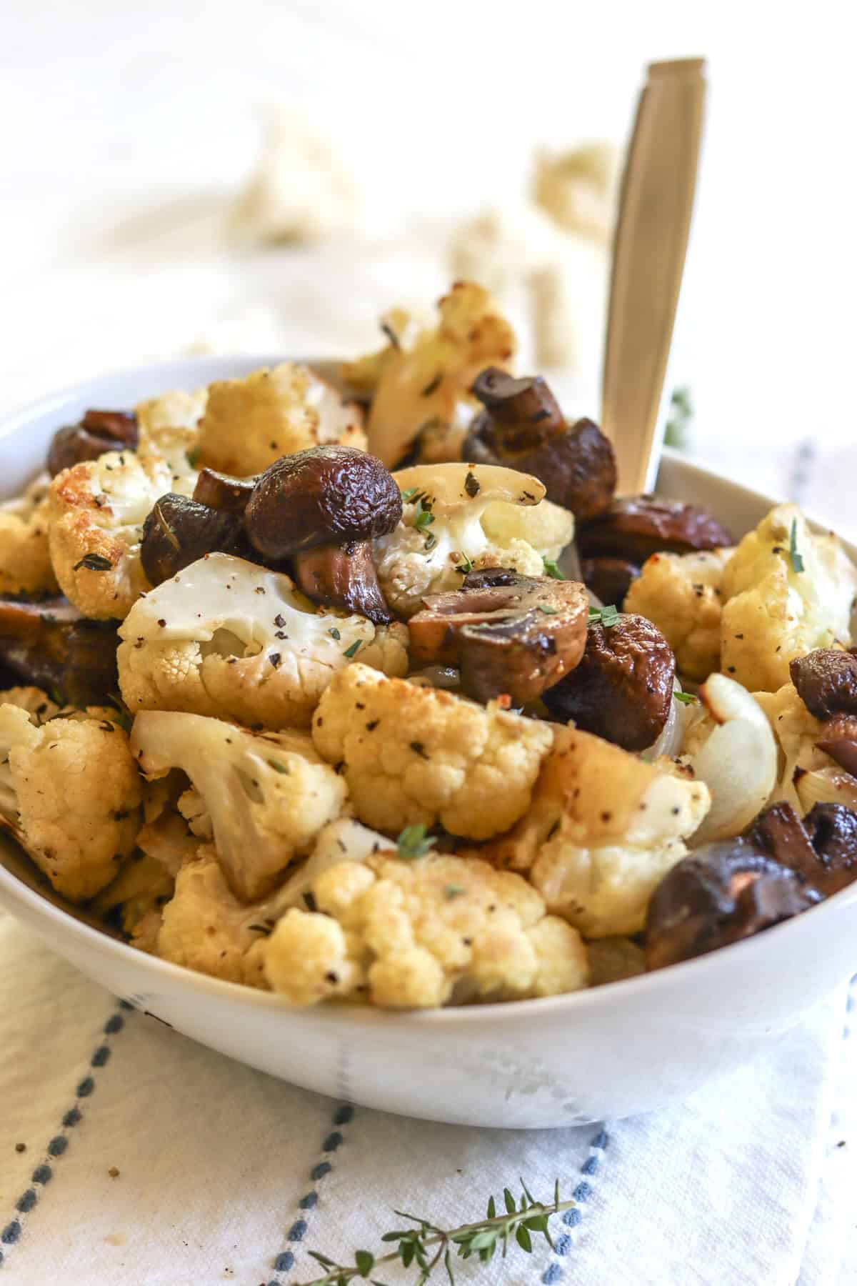 A white oval serving dish of cauliflower and mushrooms and fresh herbs with onions.