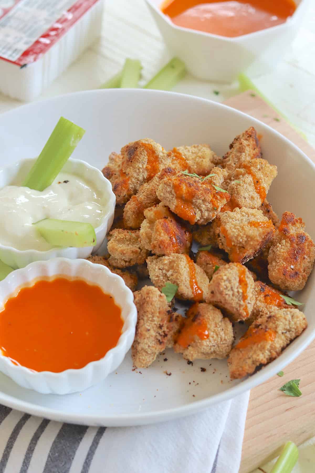 A white plate bowl piled with crispy buffalo tofu wings with a side of buffalo sauce and blue cheese dressing.