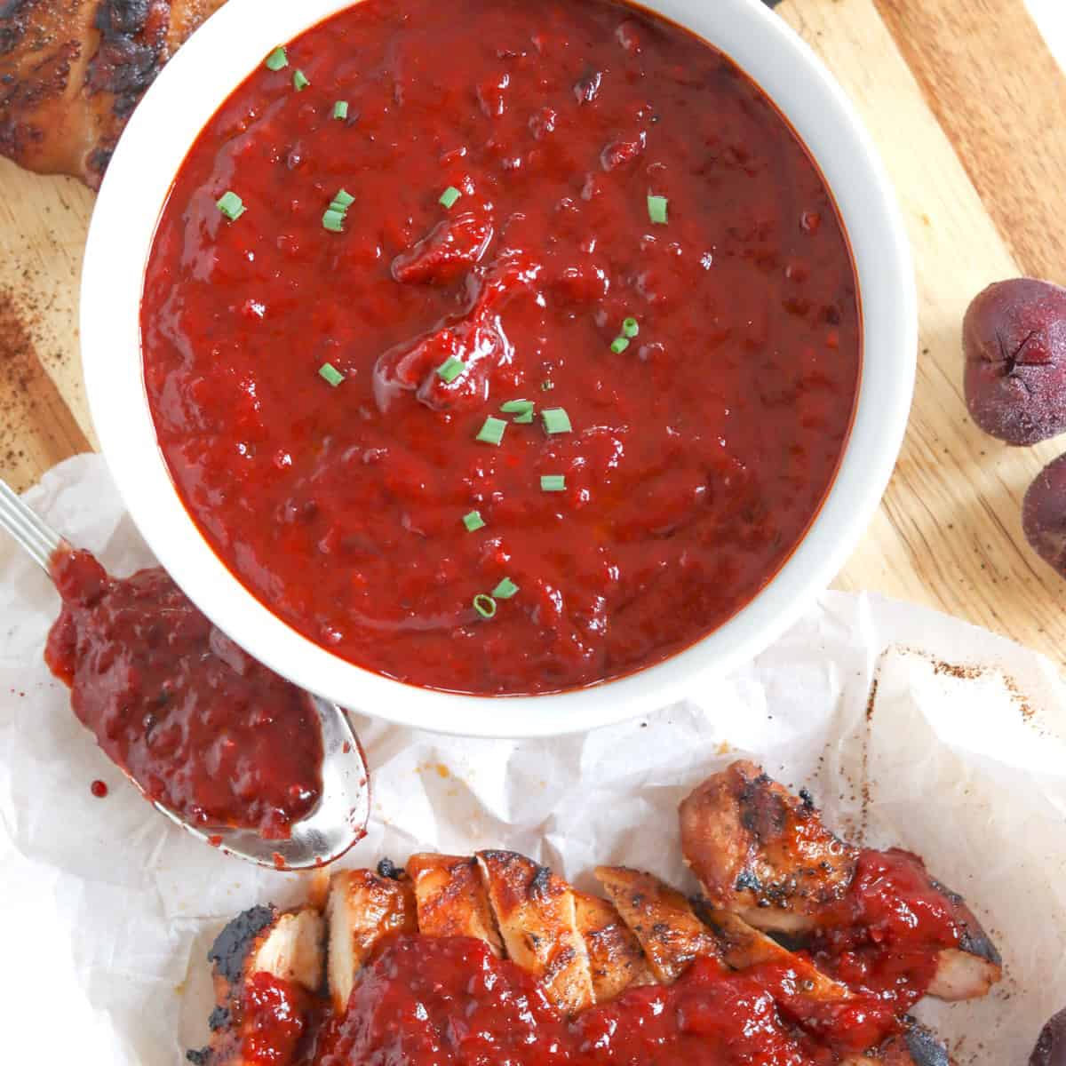 Cherry bbq sauce in a white bowl with grilled sliced chicken on the side.