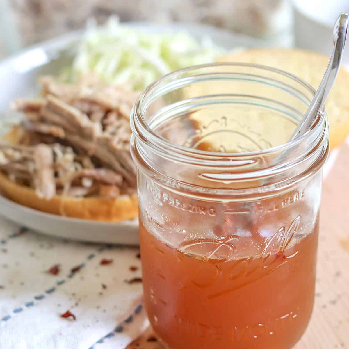 A clear glass canning jar of vinegar based eastern carolina bbq sauce beside bbq pulled pork.