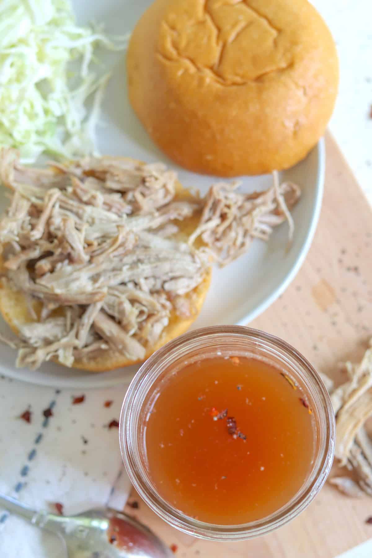 A clear mason jar of eastern carolina bbq sauce with pulled pork on a bun.