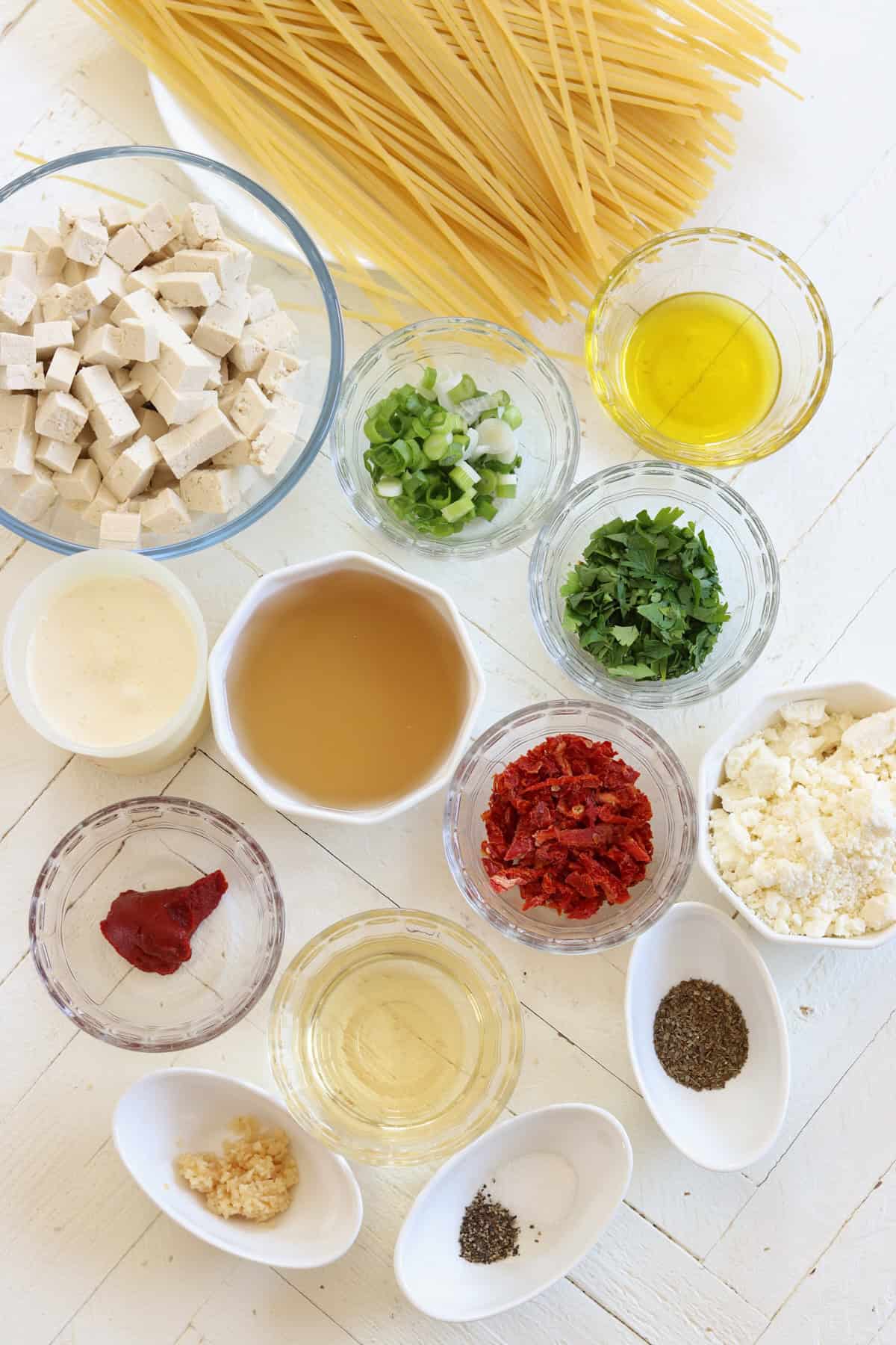 ingredients needed for making marry me tofu pasta on a white wooden board.