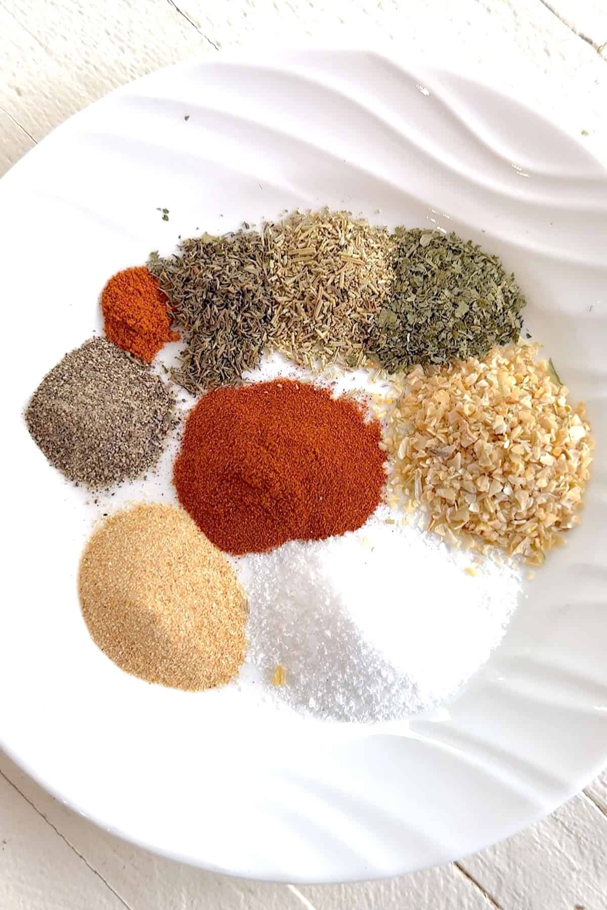 All the ingredients needed for making Montreal chicken seasoning on a white plate.
