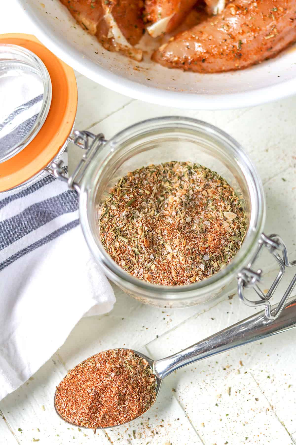 A lidded clear jar full of Montreal chicken seasoning mix.