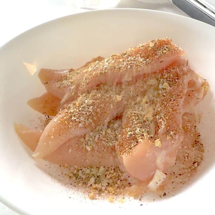 Sprinkling Montreal chicken seasoning over chicken breast tenders.