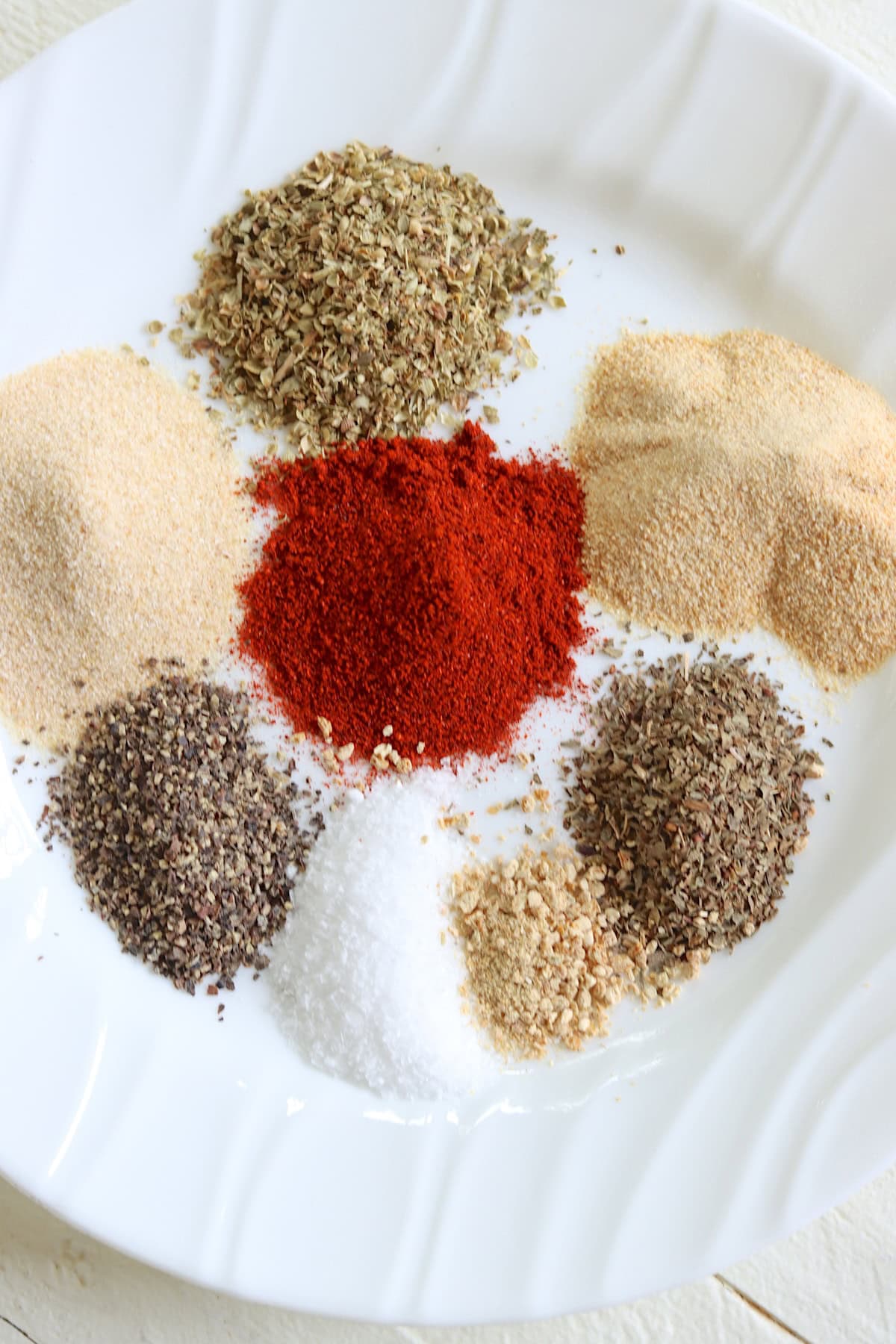 Dried herbs and seasonings on a white plate.