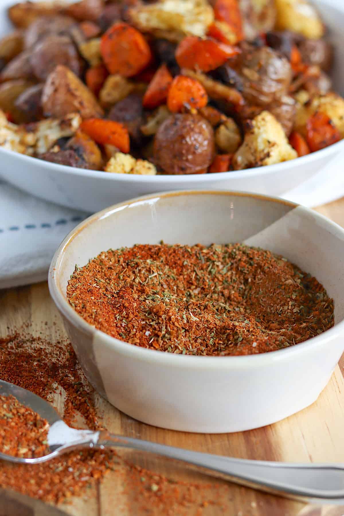 Homemade vegetable seasoning mix in a small white bowl and roasted vegetables on a platter.