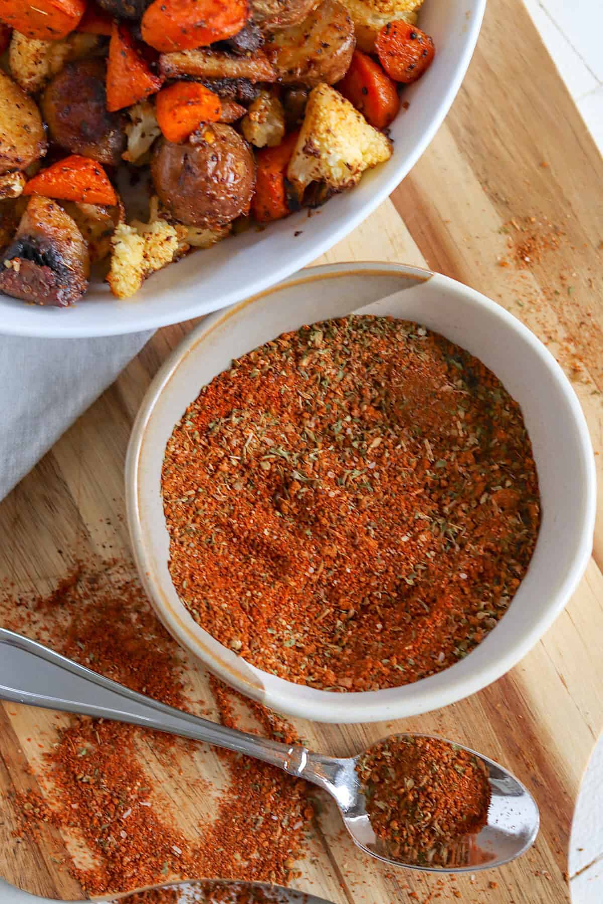 A white bowl of roasted vegetable seasoning mix with a spoon on a wooden board.