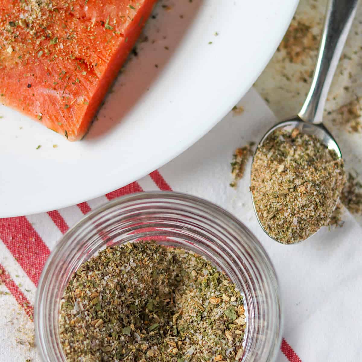 Seafood seasoning in a clear glass jar with a salmon fillet in the background.