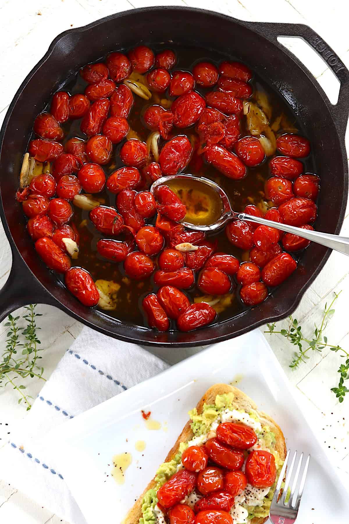 A cast iron skillet of cherry tomatoes confit and a slice of avocado toast with ricotta.