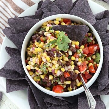 Corn and black bean salsa served in a white bowl with a blue tortilla chip.