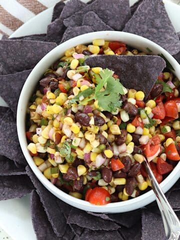 Corn and black bean salsa served in a white bowl with a blue tortilla chip.