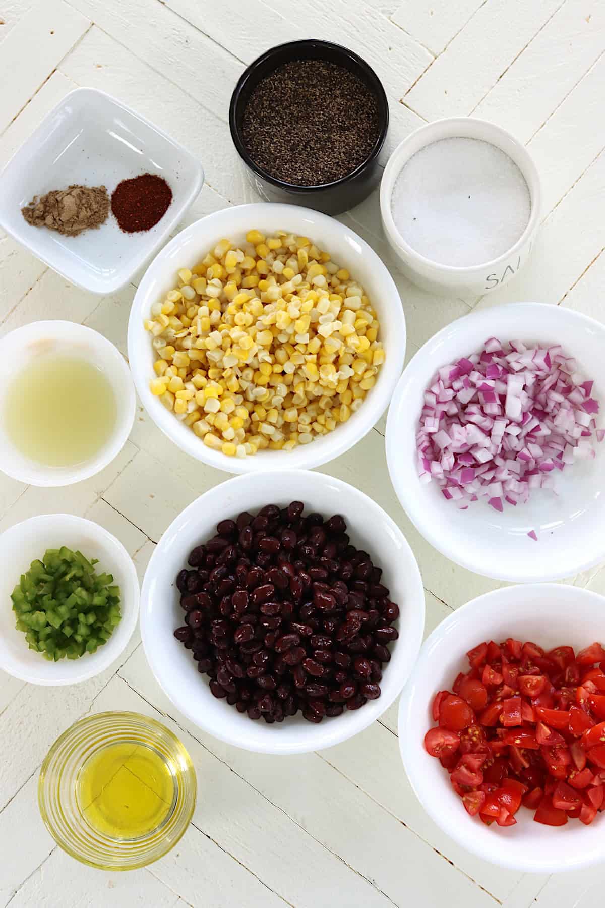 Ingredients needed for making corn and black bean salsa on a white wooden board.