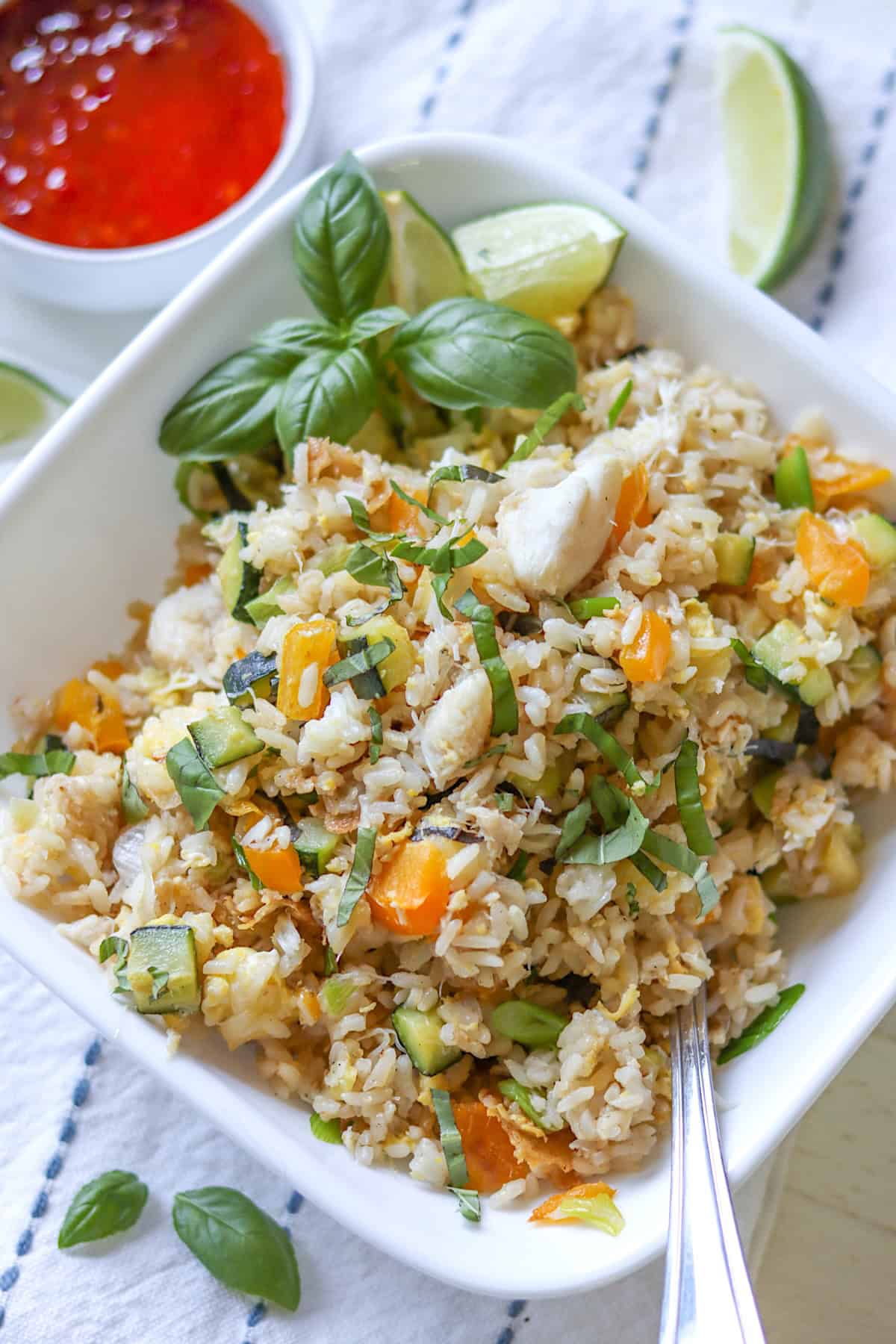 A white square bowl of crab fried rice with a side of Thai sweet chili sauce.